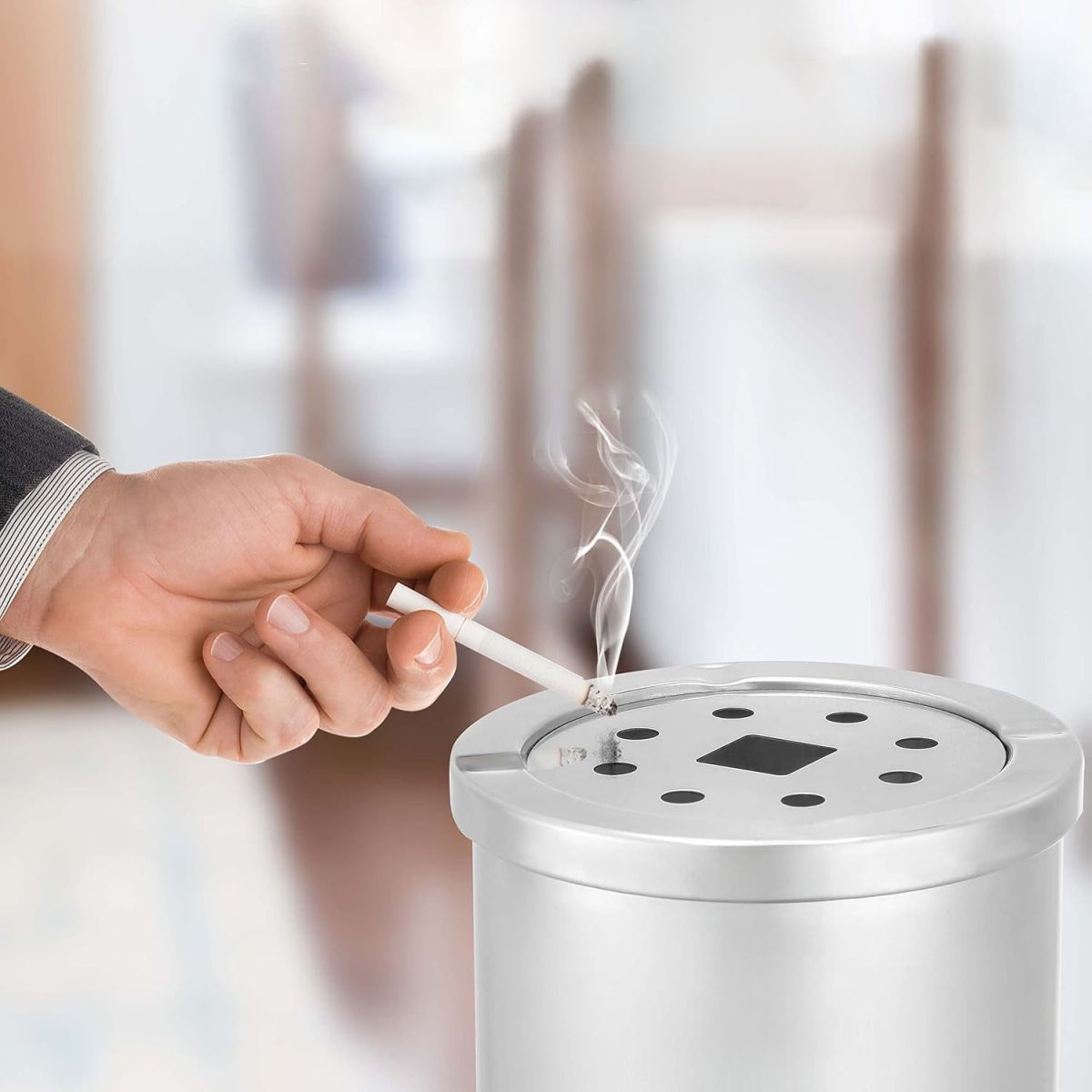 Hand holding lit cigarette over stainless steel outdoor free standing ashtray
