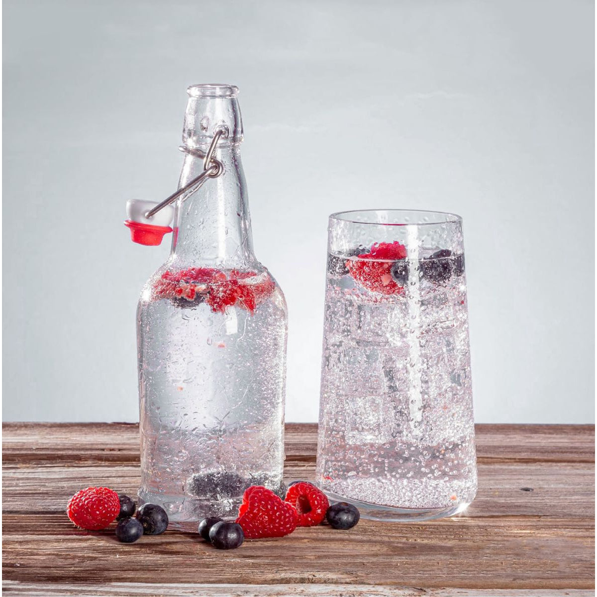 Clear glass bottle and tall glass filled with sparkling water and berries for reusable hydration