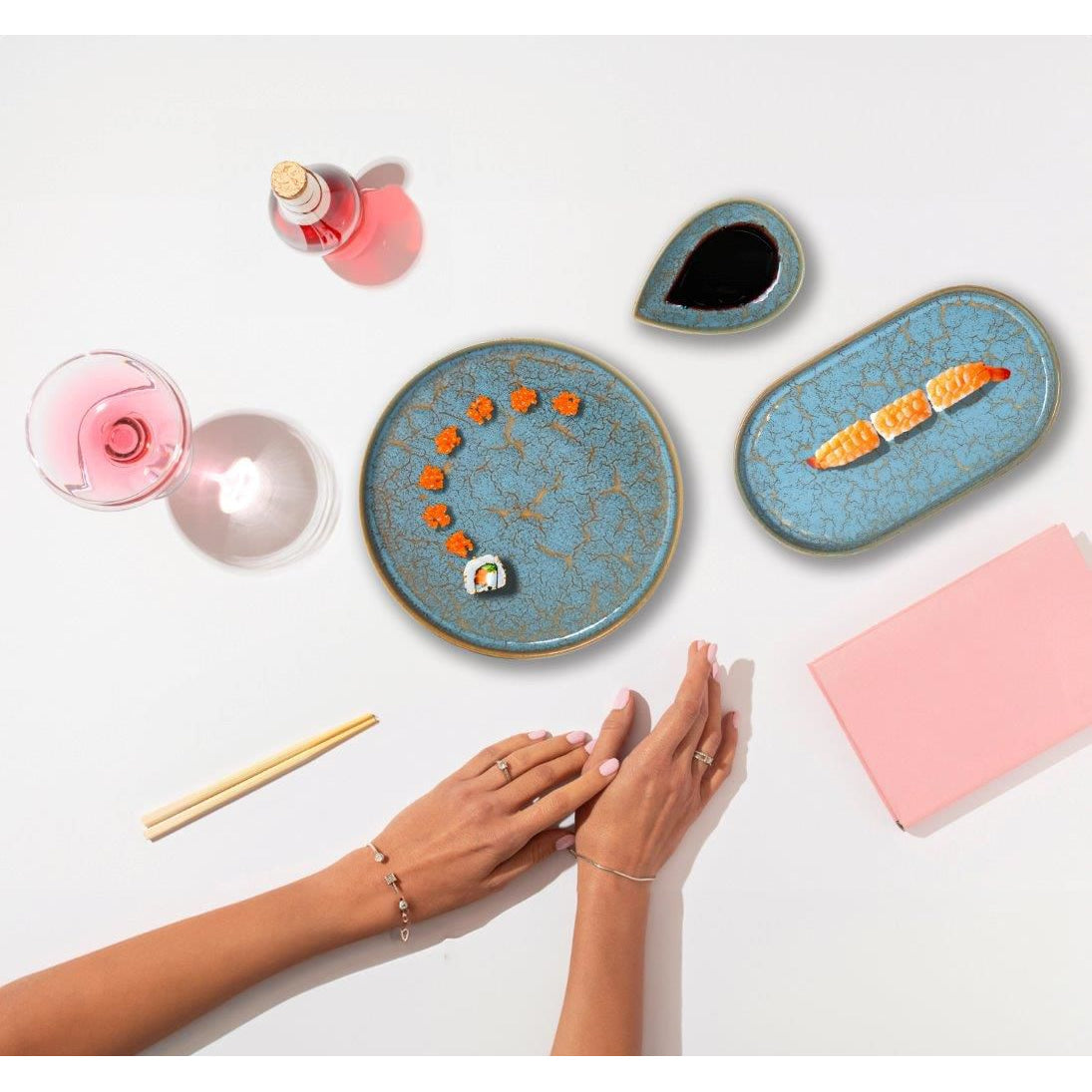 Blue and gold-rimmed ceramic Sushi dishes with chopsticks, rosé, wine, and a pink notebook