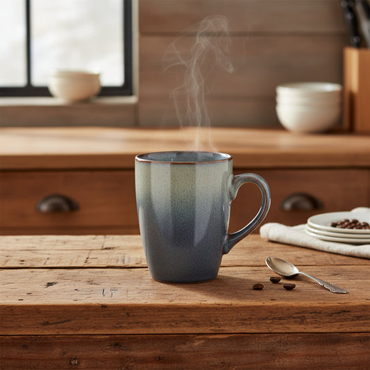 A ceramic coffee mug with a speckled gray and white glaze that transitions to a dark charcoal base, featuring a small black square logo with a white 'm' and '10 ans anniversaire' printed on the front. The mug has a C-shaped handle and a subtle copper-brown rim, shown against a plain white background.