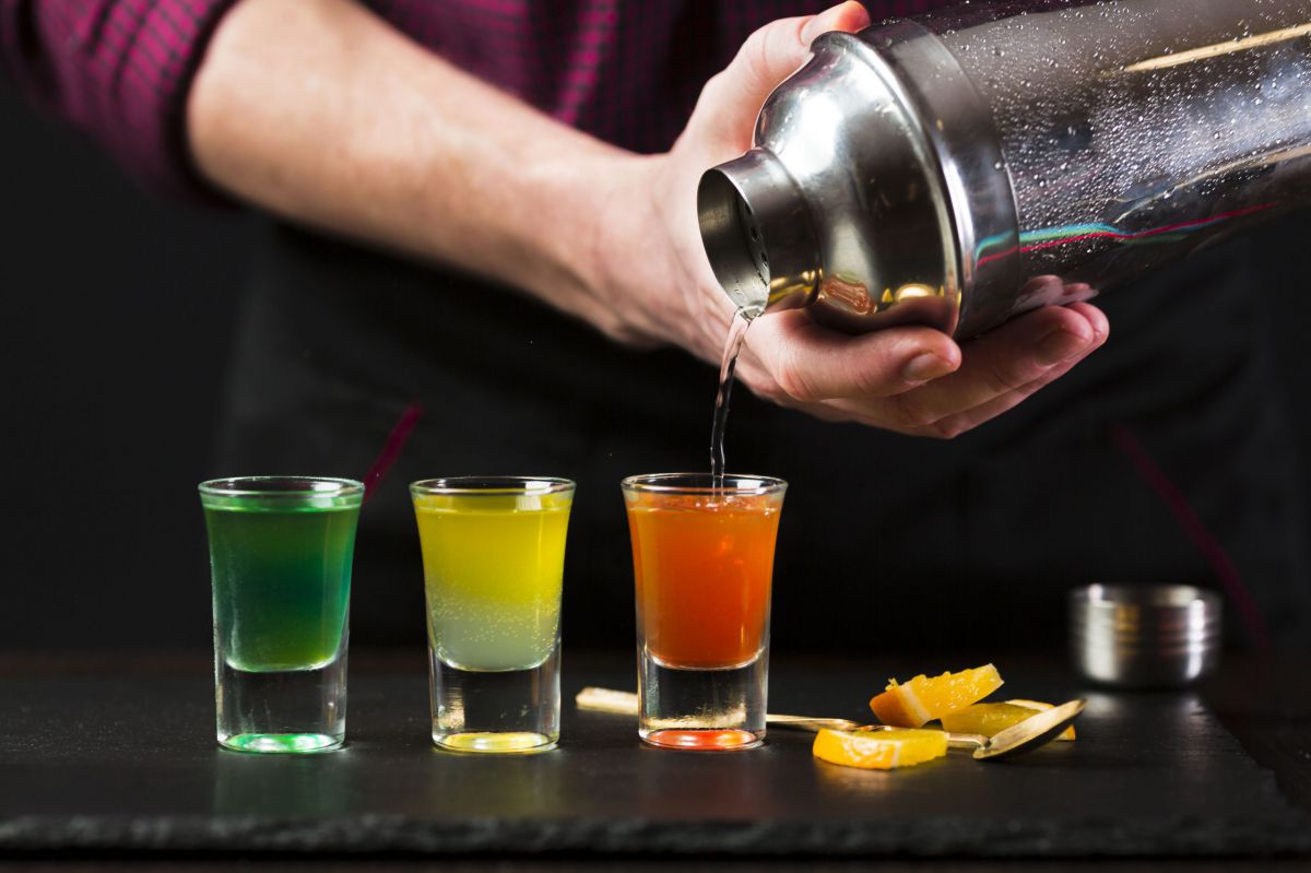 Bartender pouring colorful cocktail from Stainless Steel Cocktail Shaker 550ml My Bar Gourmet into shot glasses