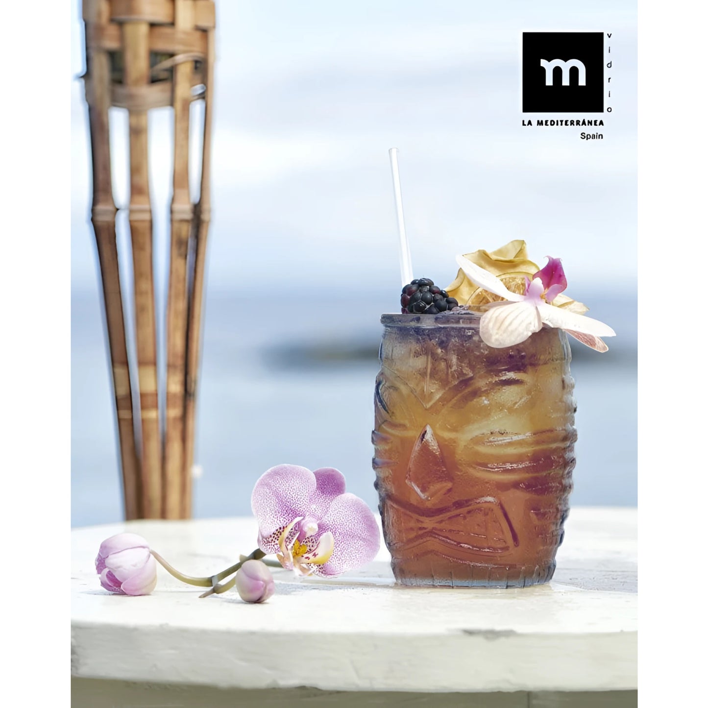 Brown carved tiki tumbler glass with golden cocktail, blackberries, orchids. Box of 6 colors